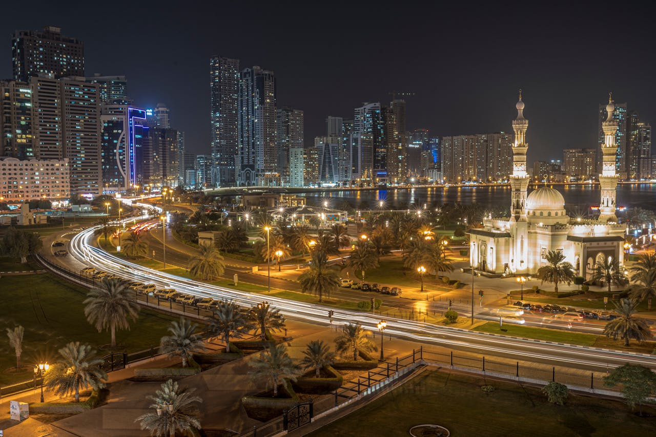 Aerial shot of Sharjah skyline at night, highlighting Al Noor Mosque and city lights.