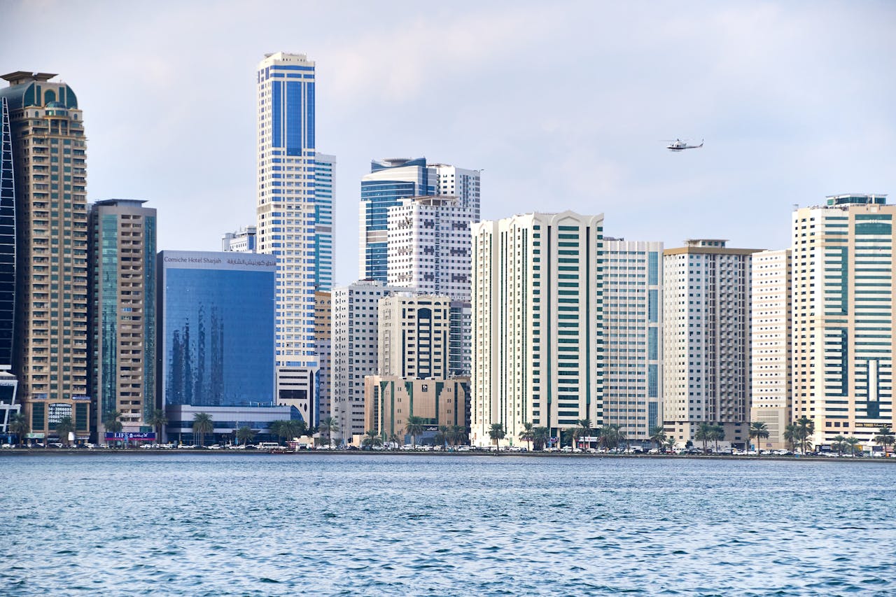 Stunning view of Al Sharjah skyline with modern skyscrapers, sea, and helicopter passing by.