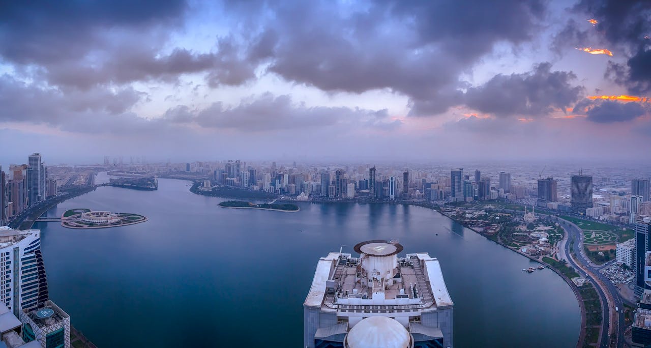 A breathtaking aerial view of Sharjah's skyline with a dramatic sky and water reflections at dusk.