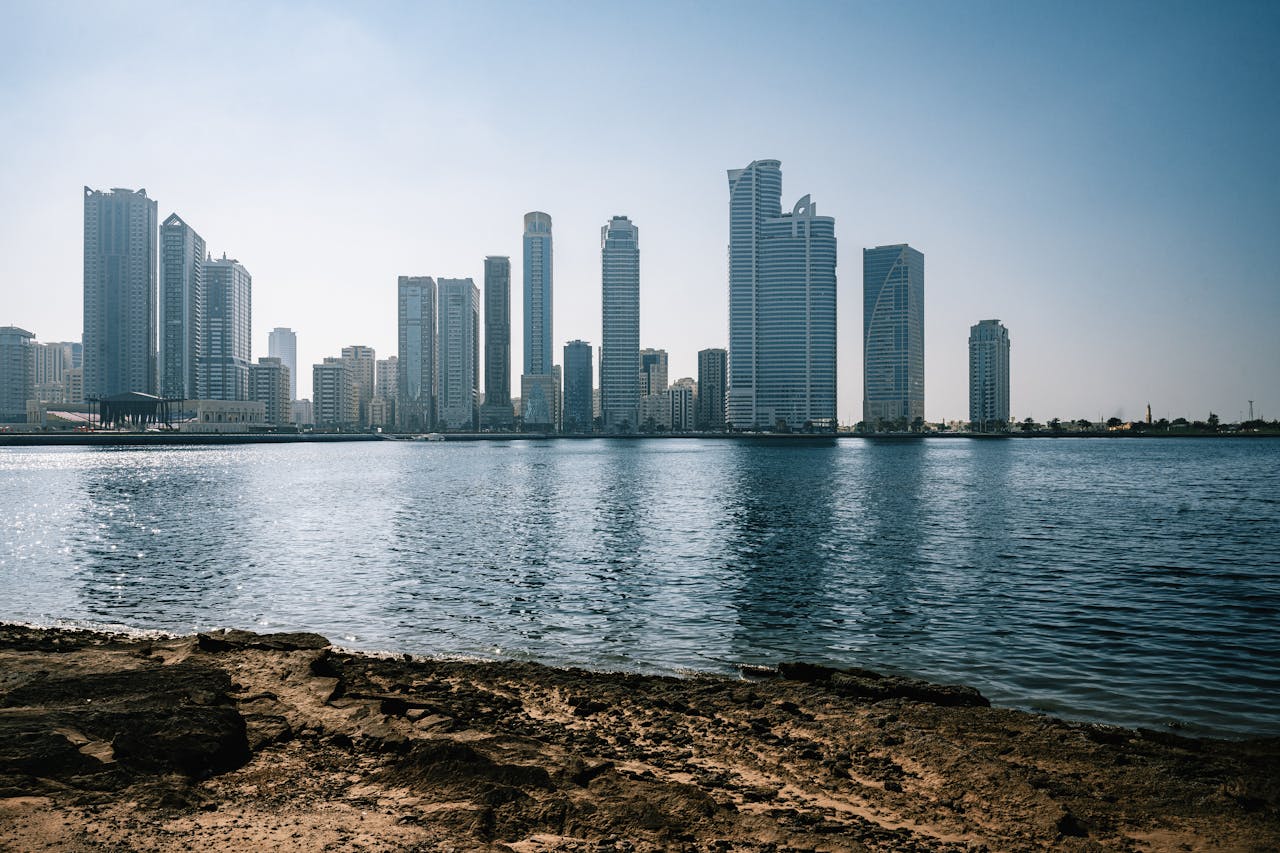 Panoramic view of Sharjah's skyline with towering skyscrapers reflecting in the water.